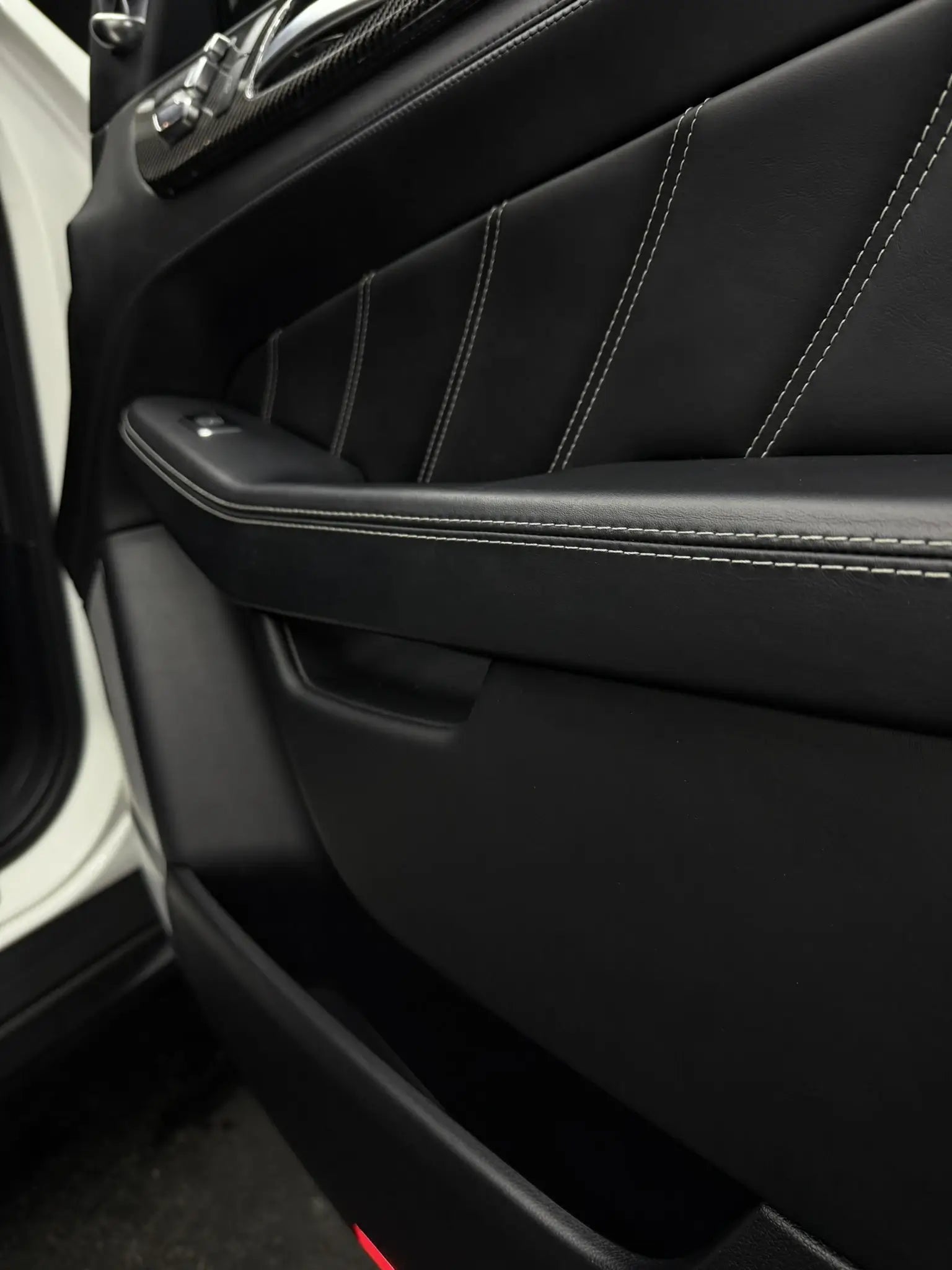 Detailaufnahme eines Fahrzeugtürinnenraums mit schwarzem Leder und feinen Nähten, ideal für Innenraumpflege.