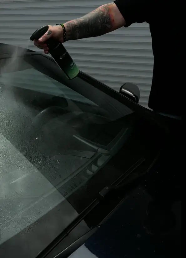 Mann sprüht Viscura Handwäsche Set auf Autoscheibe zur Reinigung und Pflege.