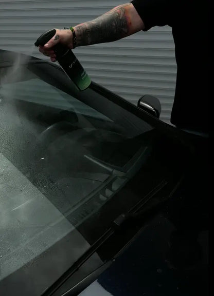 Mann sprüht Viscura Handwäsche Set auf Autoscheibe zur Reinigung und Pflege.