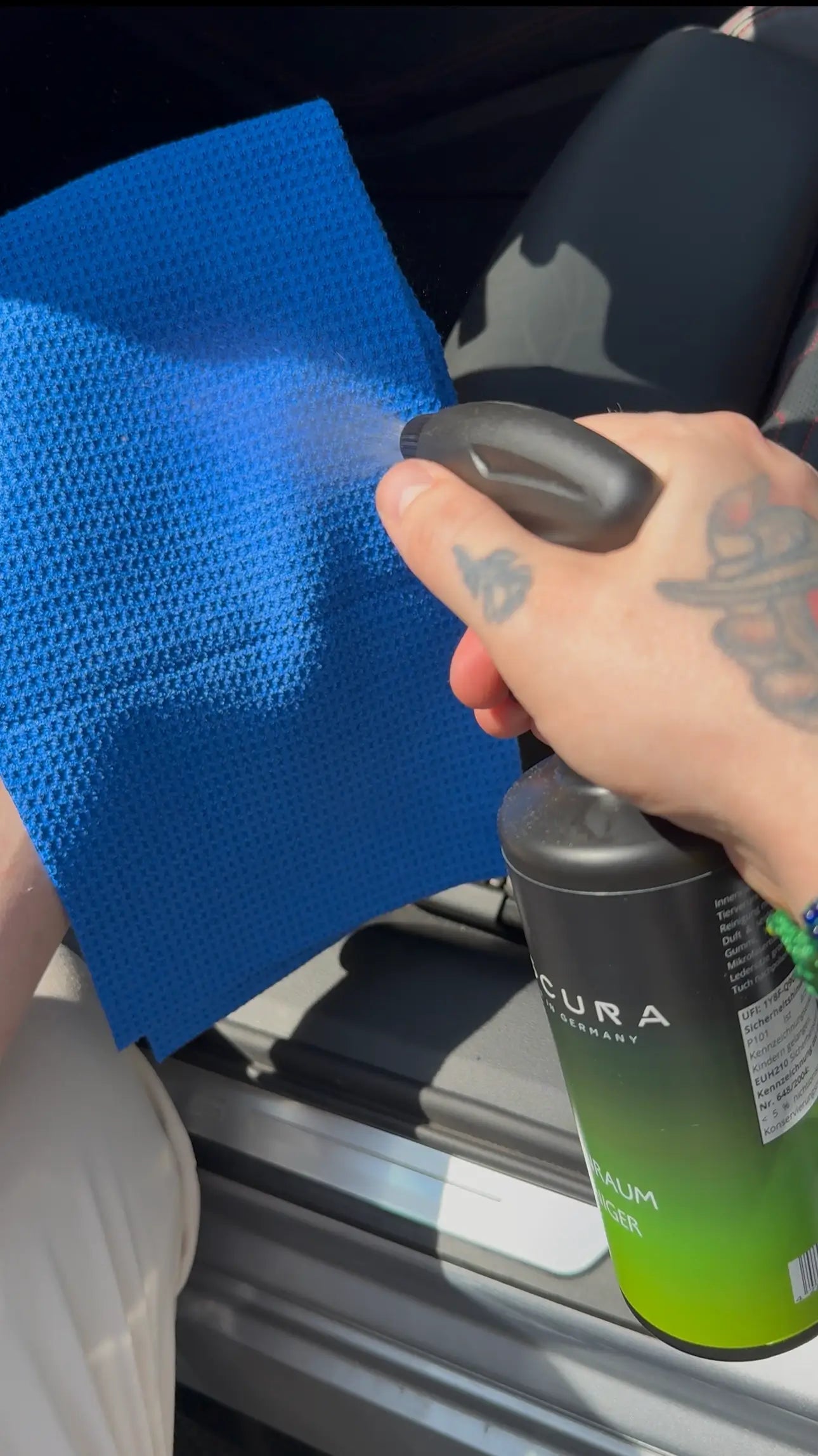 Person using Viscura cleaning spray on a blue cloth for vehicle interior care.