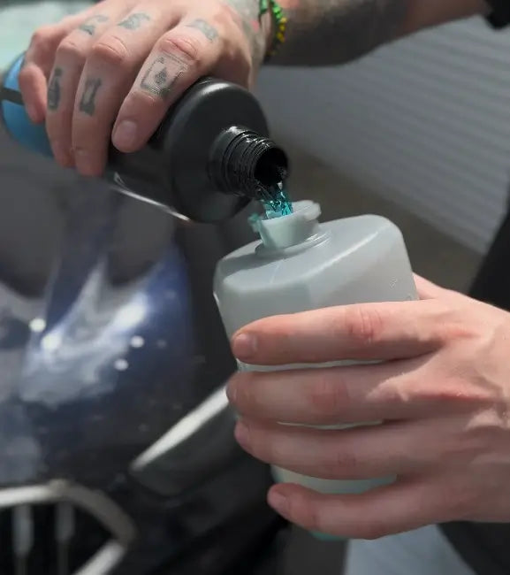 Person pouring Viscura Wax Shampoo into a dosing bottle for effective car maintenance.